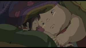 Chihiro hiding and comforting Yubaba's giant baby, Boh, in a close-up scene from Spirited Away.